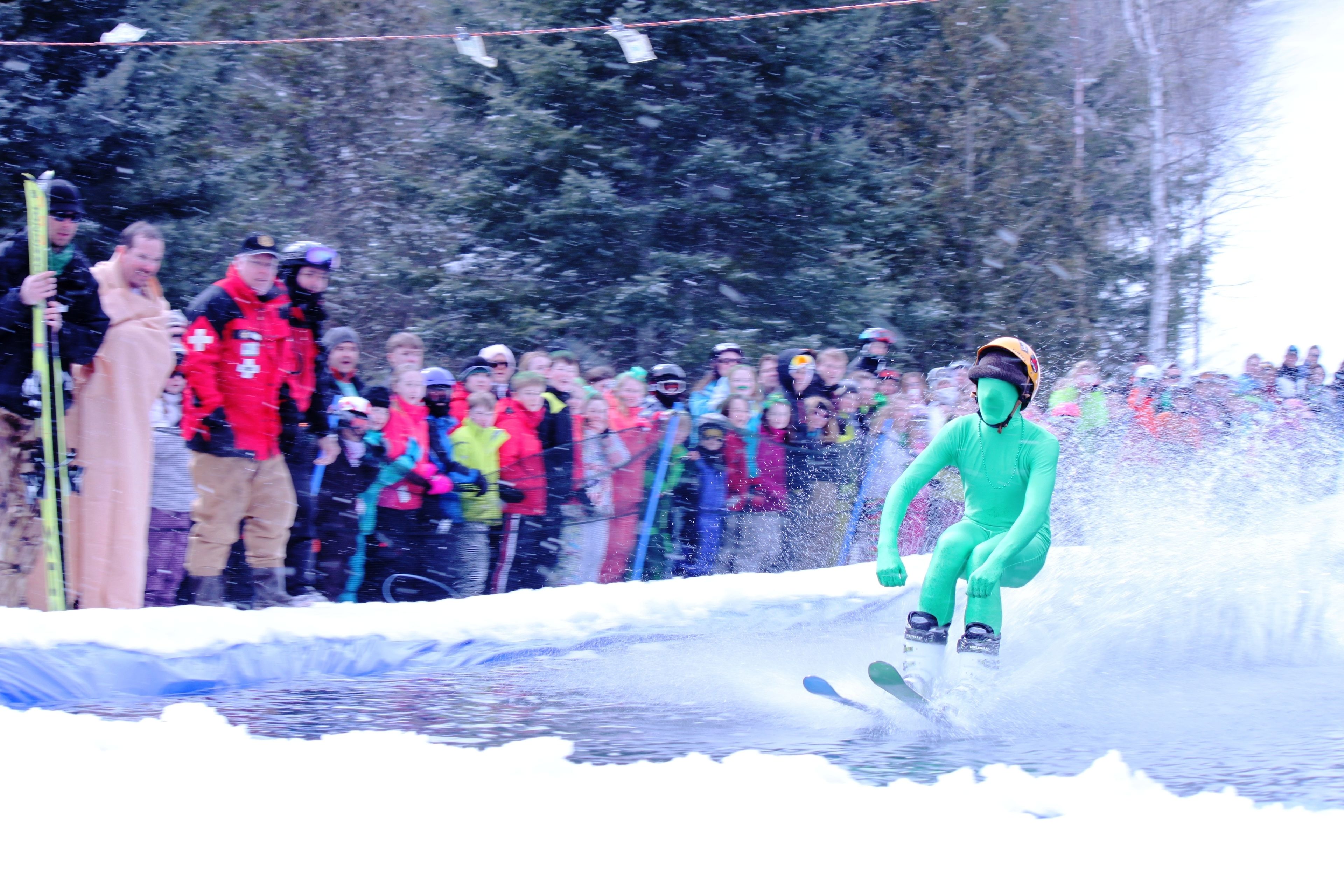 A person skiing on a snowy slope with spectators in the background.