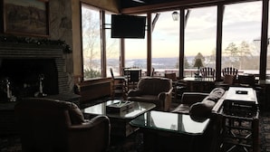 A cozy living room with a fireplace, comfortable seating, and large windows offering a scenic view. - Otsego Resort (Gaylord)