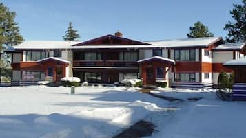 Un edificio de dos pisos con fachada roja y blanca, un acceso cubierto y una entrada a la cochera cubierta de nieve.