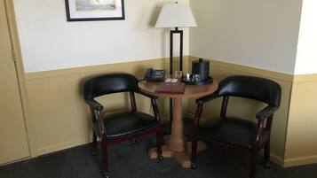 Una habitación de esquina con dos sillones de cuero negro, una mesita redonda con lámpara, un teléfono y una cafetera.