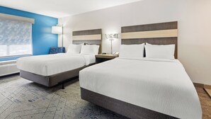 A hotel room with two beds, a nightstand with a lamp, a window with blinds, and a wall-mounted light fixture.