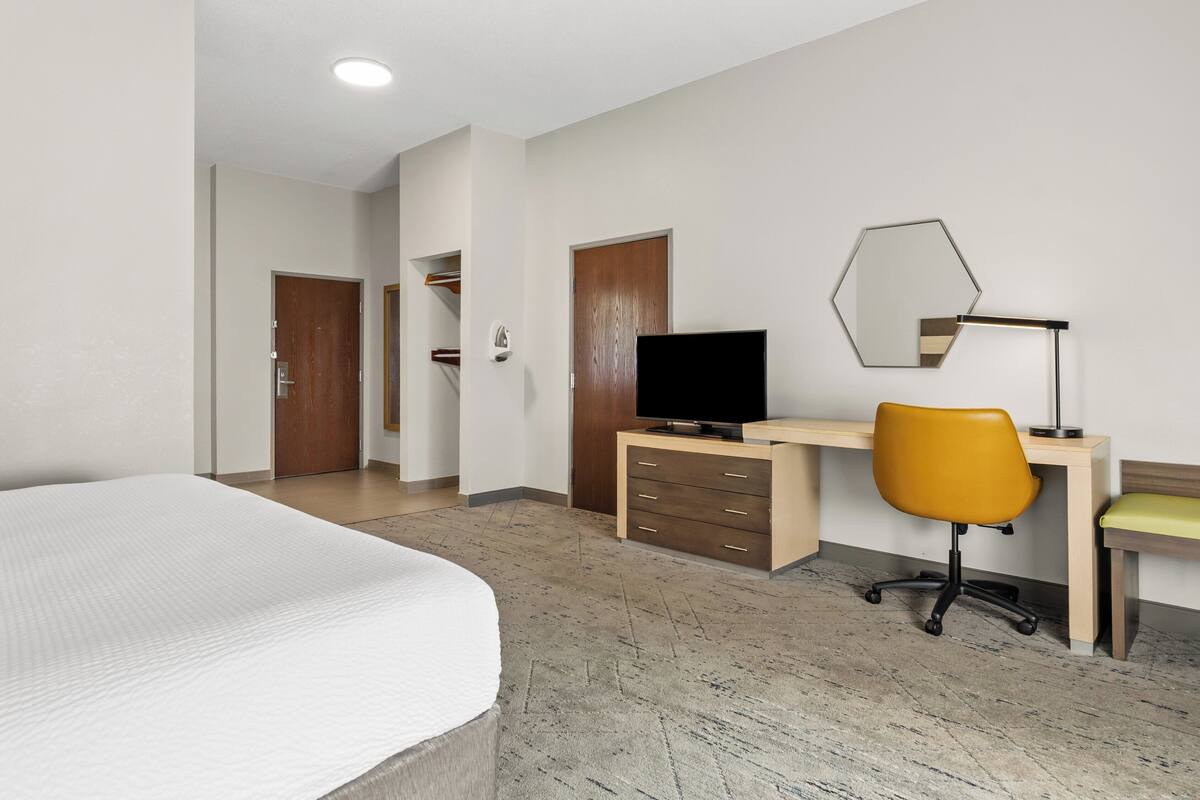 Una habitació d'hotel amb un llit, un escriptori amb una cadira, una televisió i un mirall a la paret.