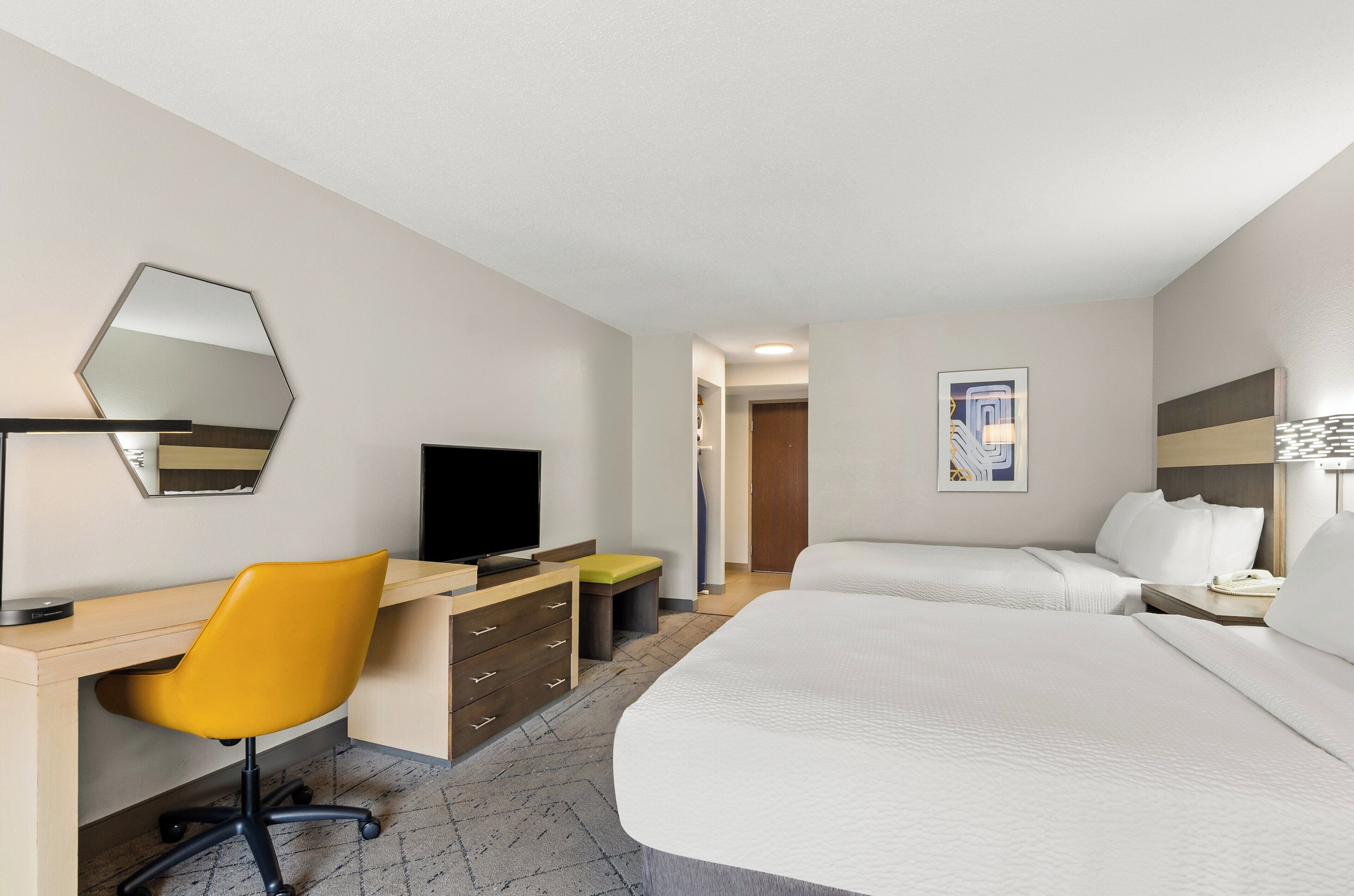 A hotel room with a bed, a desk with a chair, a television, a dresser, and a mirror.