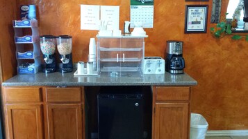 Una encimera de cocina con una cafetera, un tostador y varios recipientes de comida.