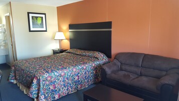 Una habitación de hotel con una cama, un sofá, una mesita de noche con lámpara y un cuadro en la pared.