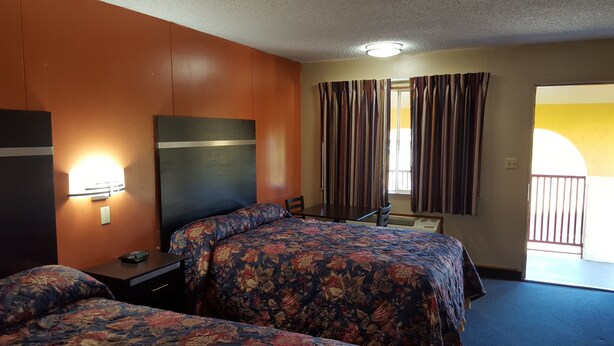 A hotel room with two beds, a desk, a chair, a nightstand, a lamp, and a window with curtains. - Carefree Inn Flatonia (Flatonia)
