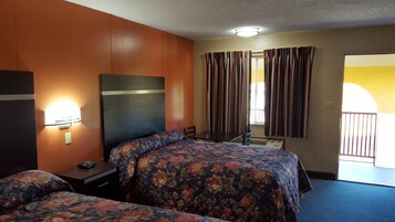 Habitación de hotel con dos camas, un escritorio, una silla, una mesita de noche, una lámpara y una ventana con cortinas.