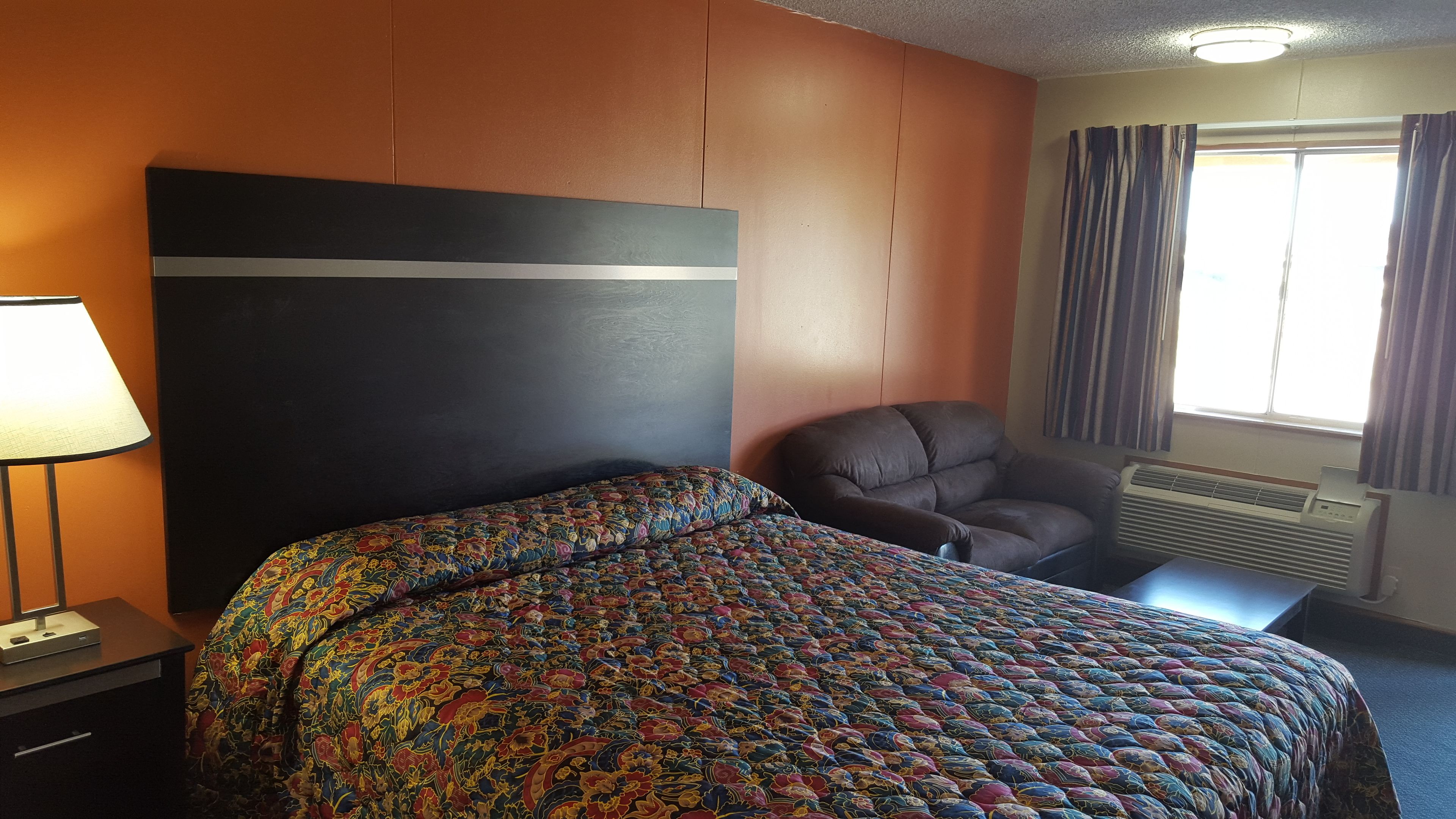 Une chambre d’hôtel avec un lit, une chaise, un bureau, une lampe et une fenêtre avec des rideaux.