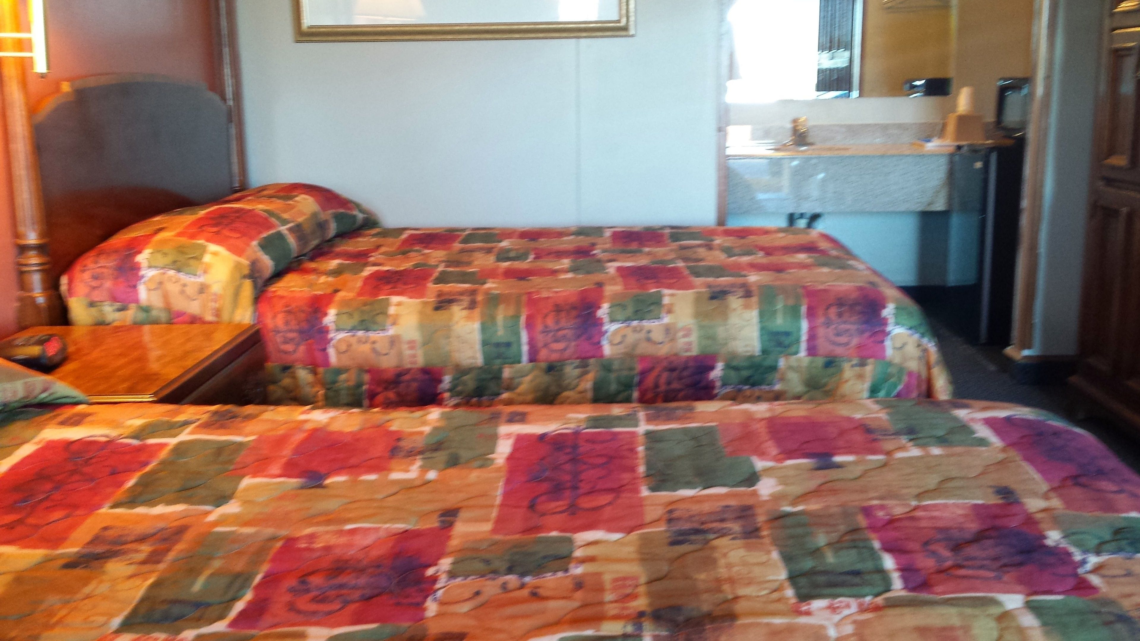 A room with a bed covered in a colorful quilt, a wooden nightstand, and a chair.