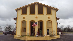 A yellow building with a flag, arched windows, and star decorations. - Carefree Inn Flatonia (Flatonia)