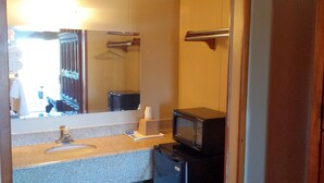 A compact hotel bathroom with a sink, mirror, towel rack, and a small refrigerator. - Carefree Inn Flatonia (Flatonia)