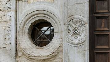 A stone window with a metal crossbar, a decorative circular emblem, and a wooden door with paneling.