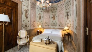 A luxurious hotel room with a large bed, ornate floral wallpaper, a chandelier, a wooden door, and a classic armchair. - Ca' Vendramin Zago (Venice)