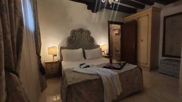 Una habitación de hotel con una cama grande, dos lámparas de noche, un candelabro y una puerta de madera.