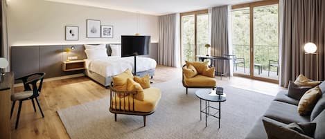 A modern hotel room with a bed, sofa, armchair, and a small table.