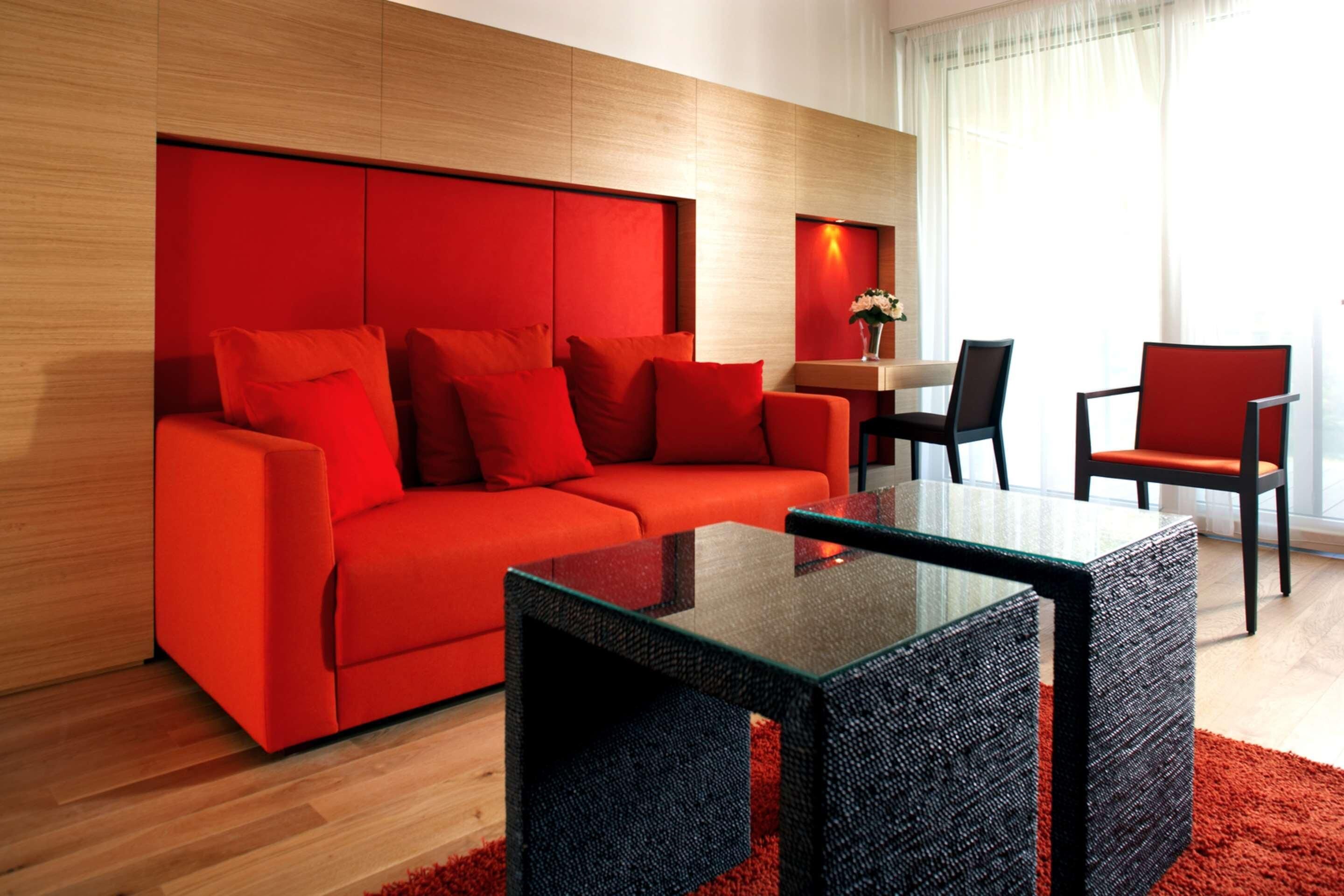 Una sala de estar moderna con un sofá rojo, sillas negras y una mesa de centro de vidrio.
