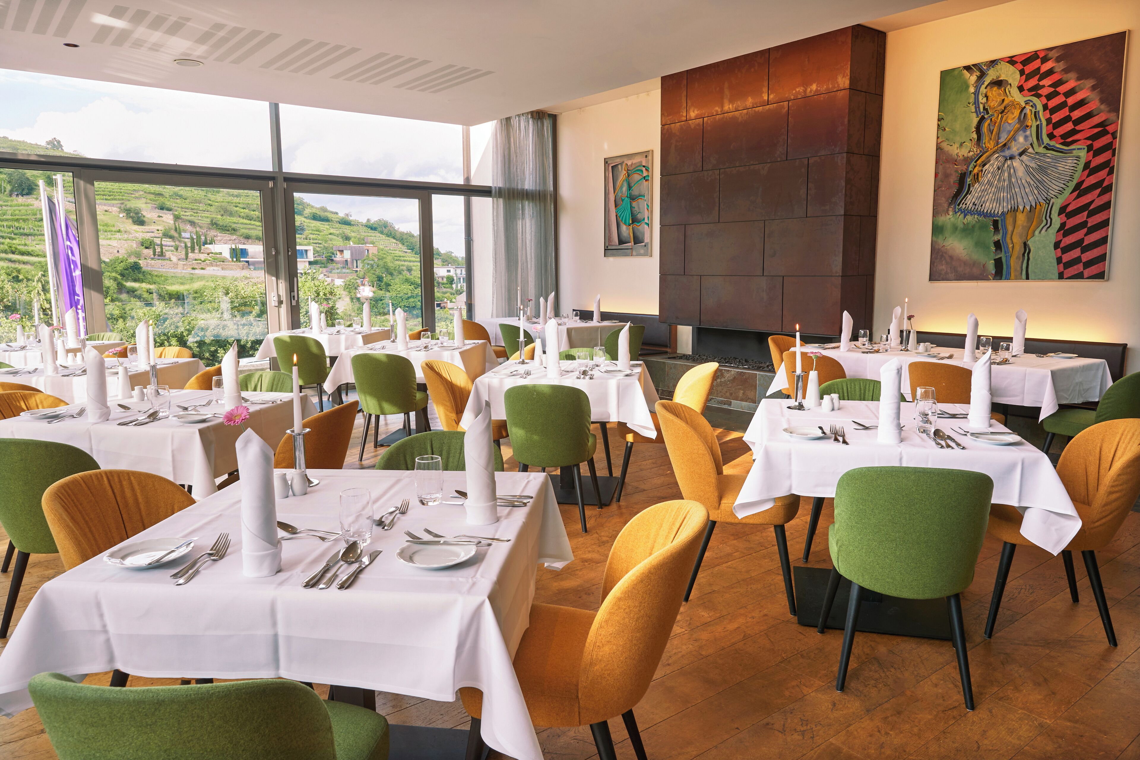 Restaurante con varias mesas preparadas para comer, ofreciendo vistas a un paisaje verde a través de amplias ventanas.