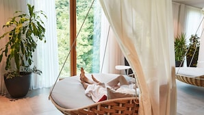 Una habitación con una silla colgante, una planta grande en maceta y vistas al verdor exterior.