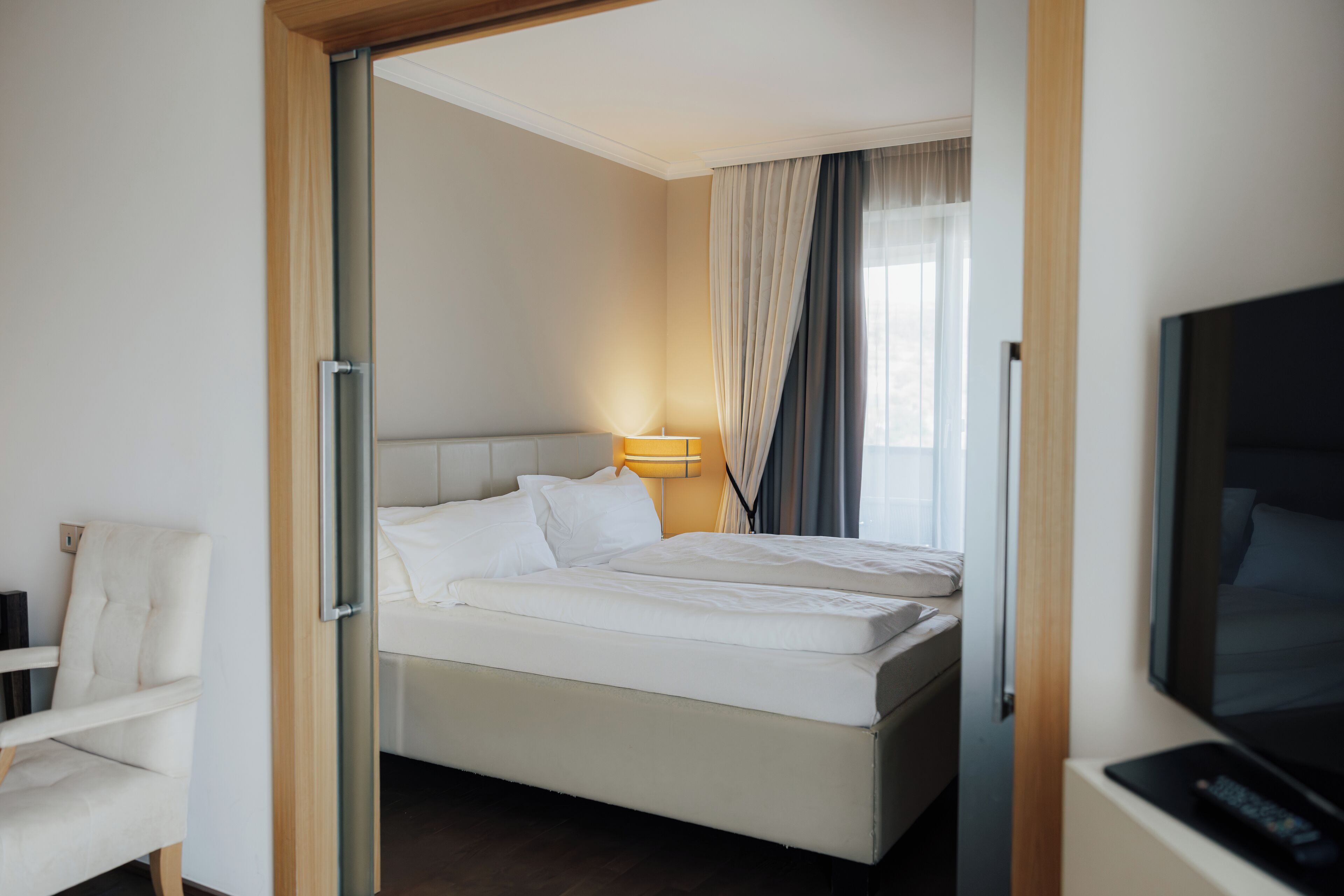 A hotel room with a bed, a chair, a TV, and a lamp.