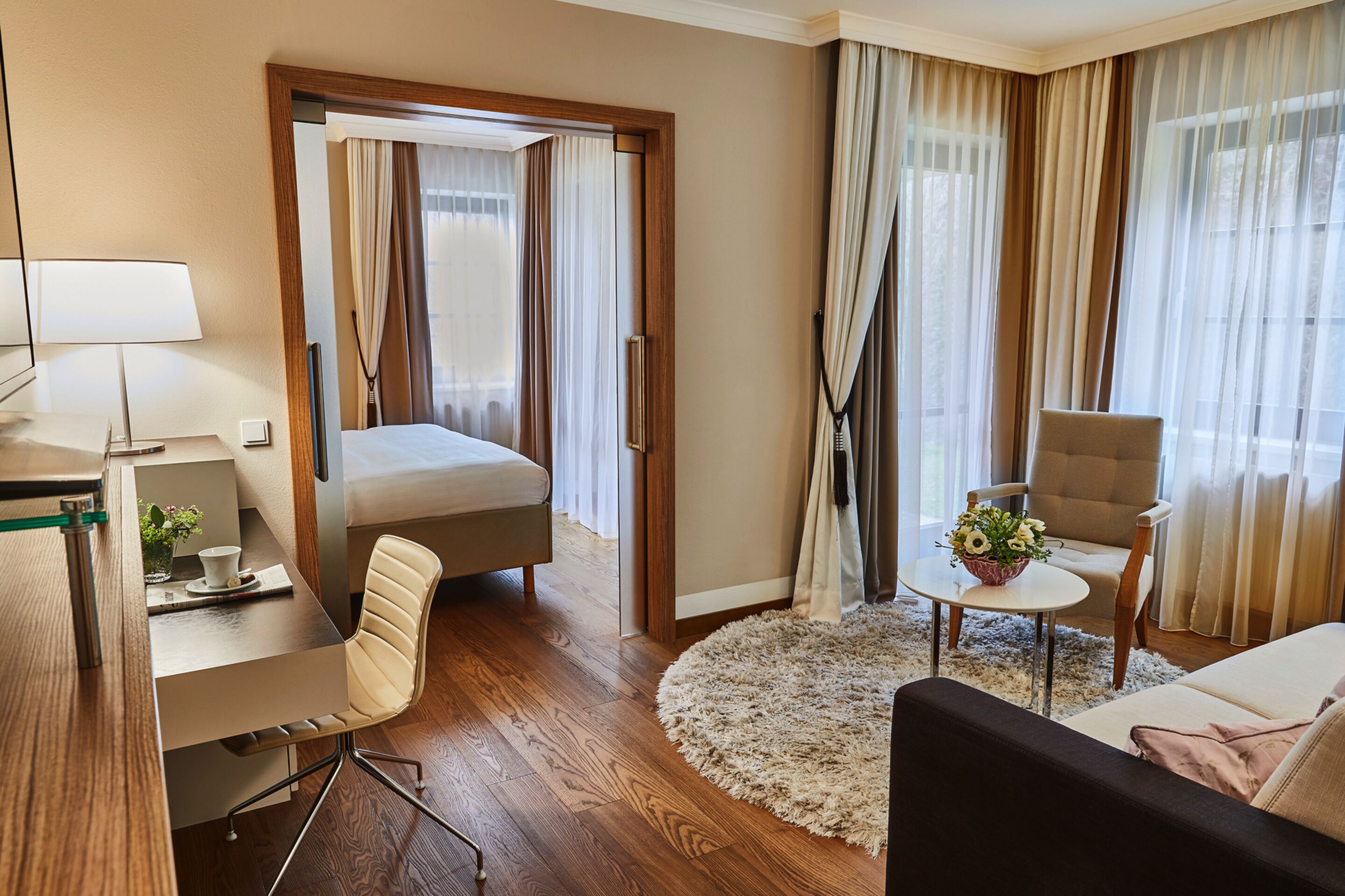 Habitación de hotel con cama, escritorio, silla, sofá y una pequeña mesa con flores.