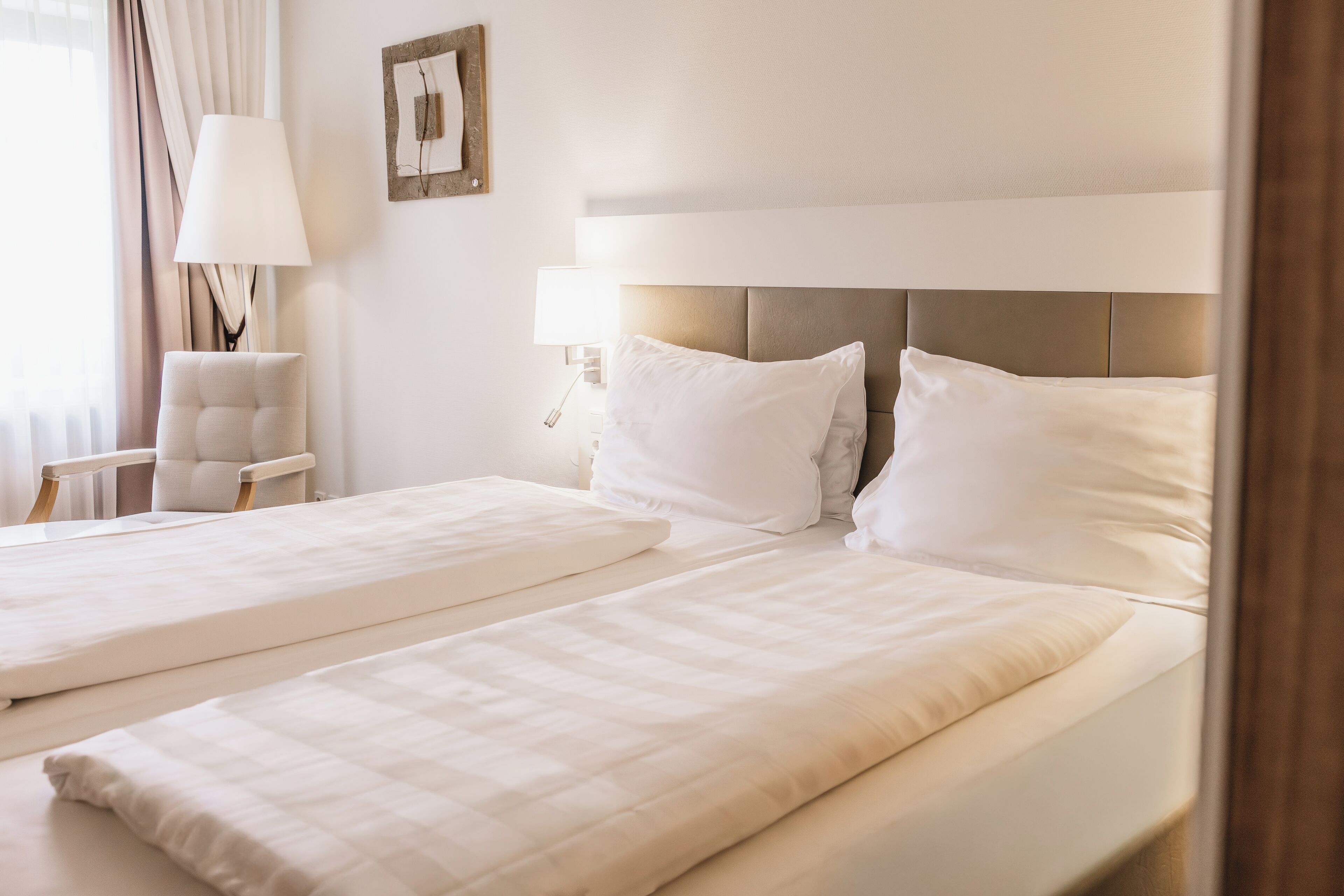 A hotel room with two beds, a chair, a lamp, and a picture on the wall.