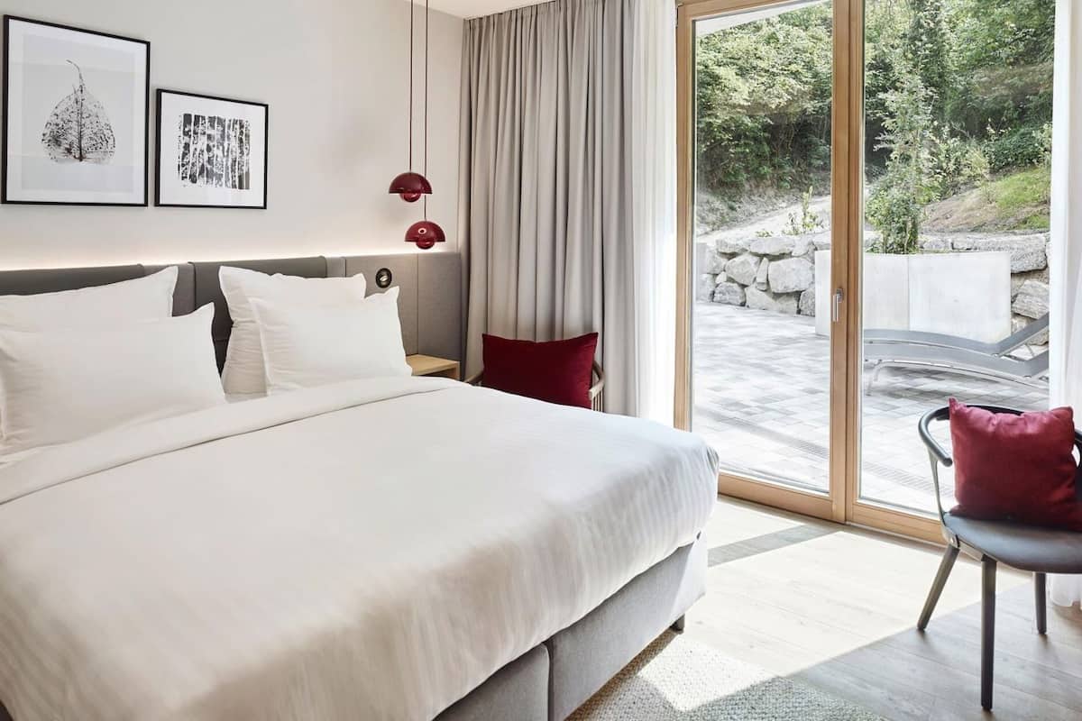 Habitación de hotel moderna con una cama grande, un escritorio, una silla y vistas al exterior.