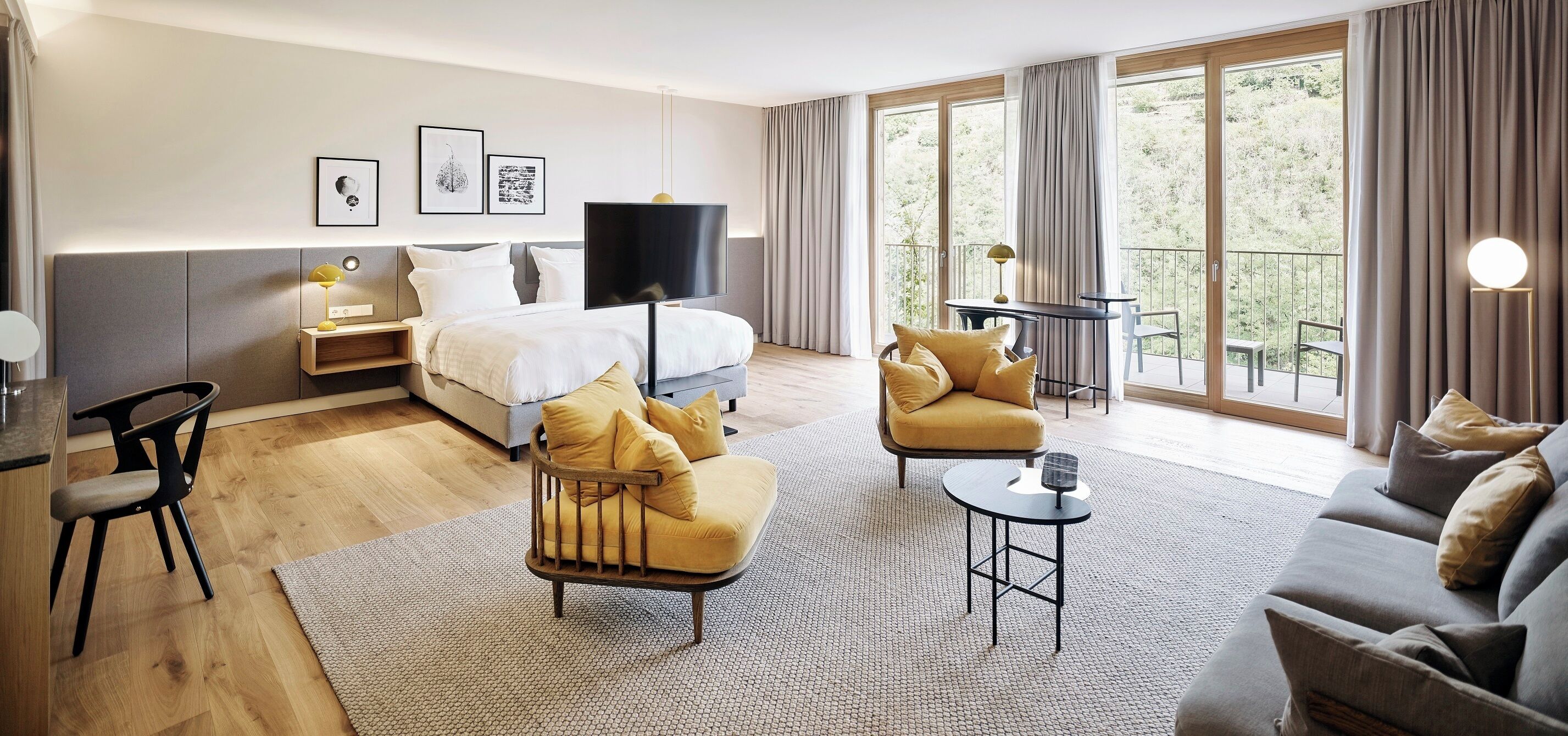 Una habitación de hotel moderna con cama, sofá, sillón, una mesita y un balcón con vistas.
