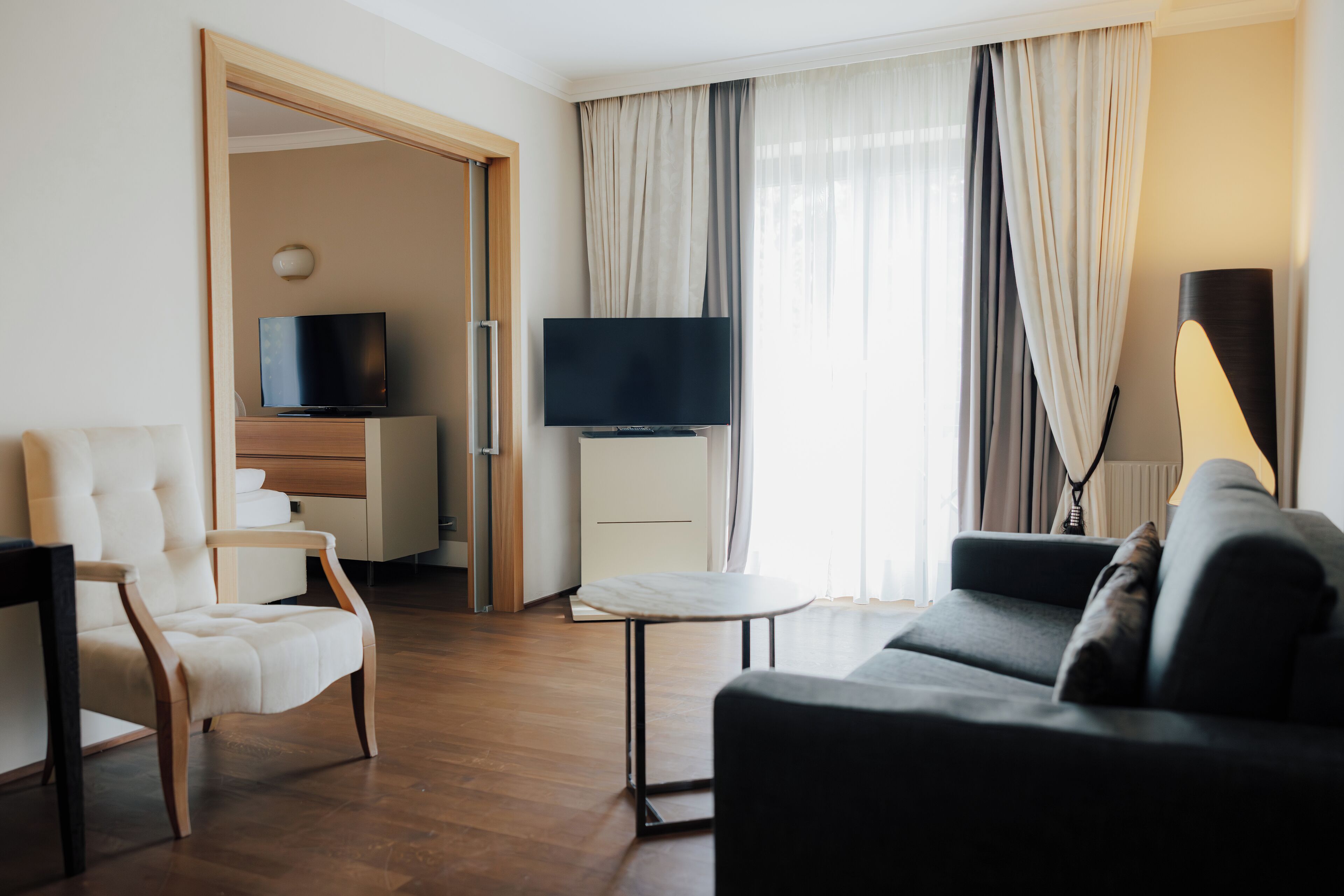 A modern hotel room with a sofa, armchair, television, and a small table.