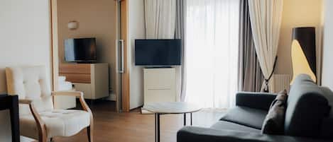 A modern hotel room with a sofa, armchair, television, and a small table.