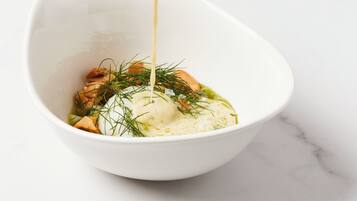 A white bowl with a creamy liquid being poured into it, containing a food item with herbs.