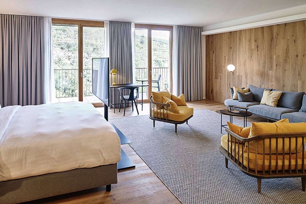 Habitación de hotel con una cama grande, un sofá, una silla y una mesita. Cuenta con un balcón con vistas al exterior.