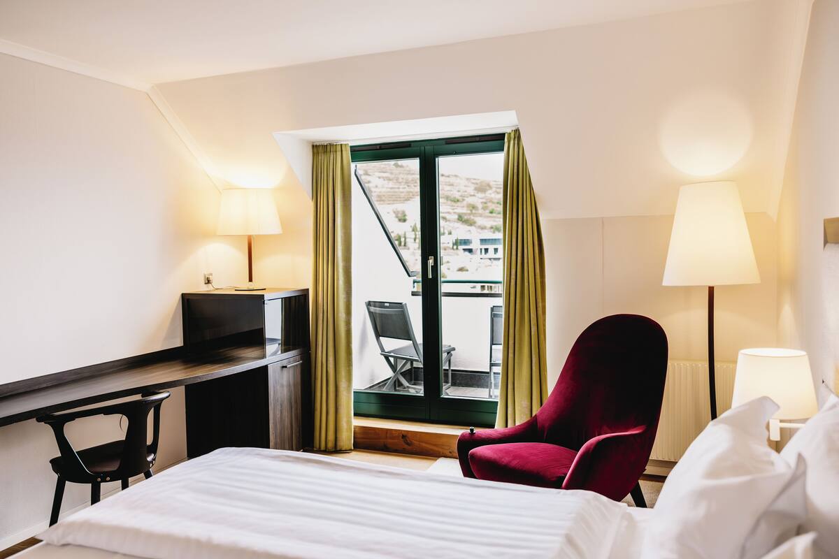 Habitación de hotel con cama, escritorio, silla y balcón con vistas.