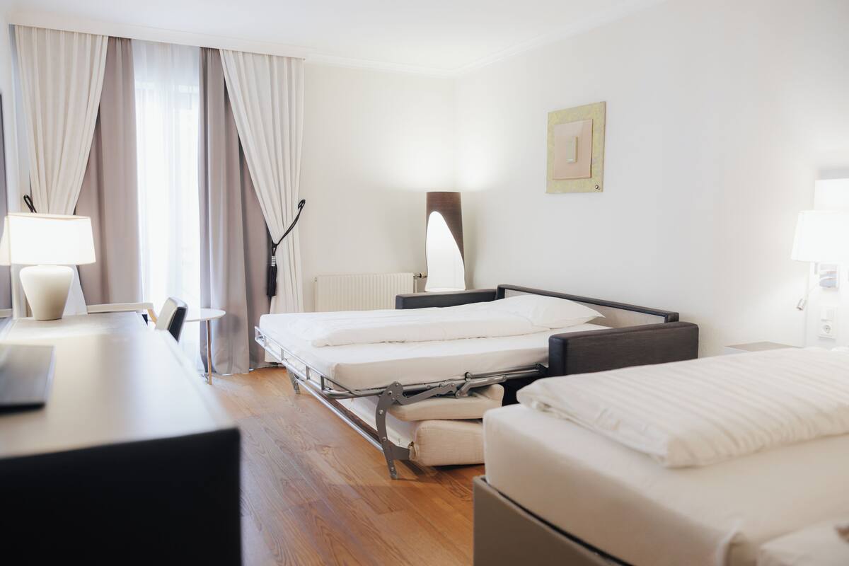 Una habitación de hotel con cama, mesita de noche, lámpara y vistas al exterior.