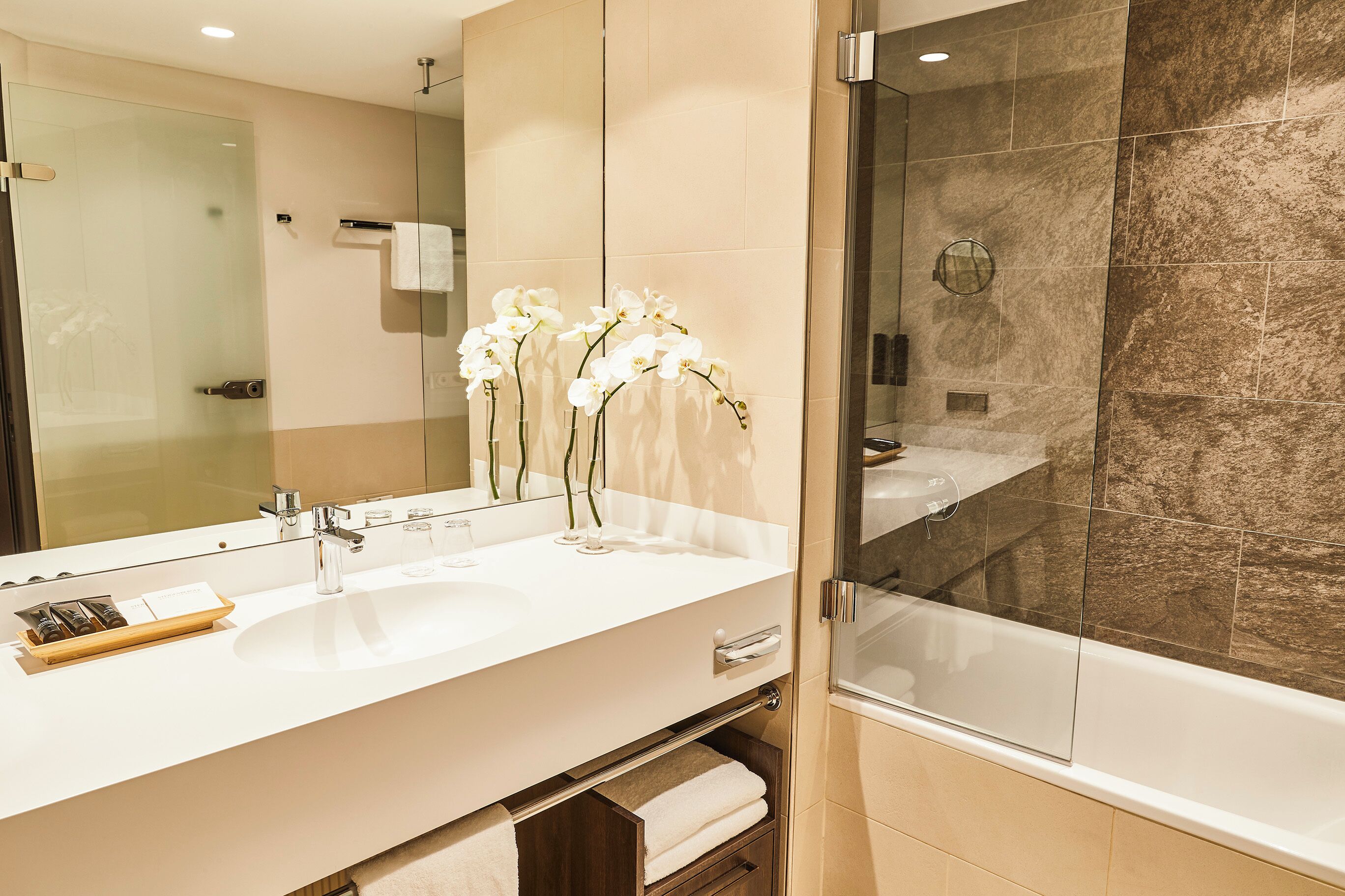 A modern bathroom with a large mirror, white sink, and a glass-enclosed shower.