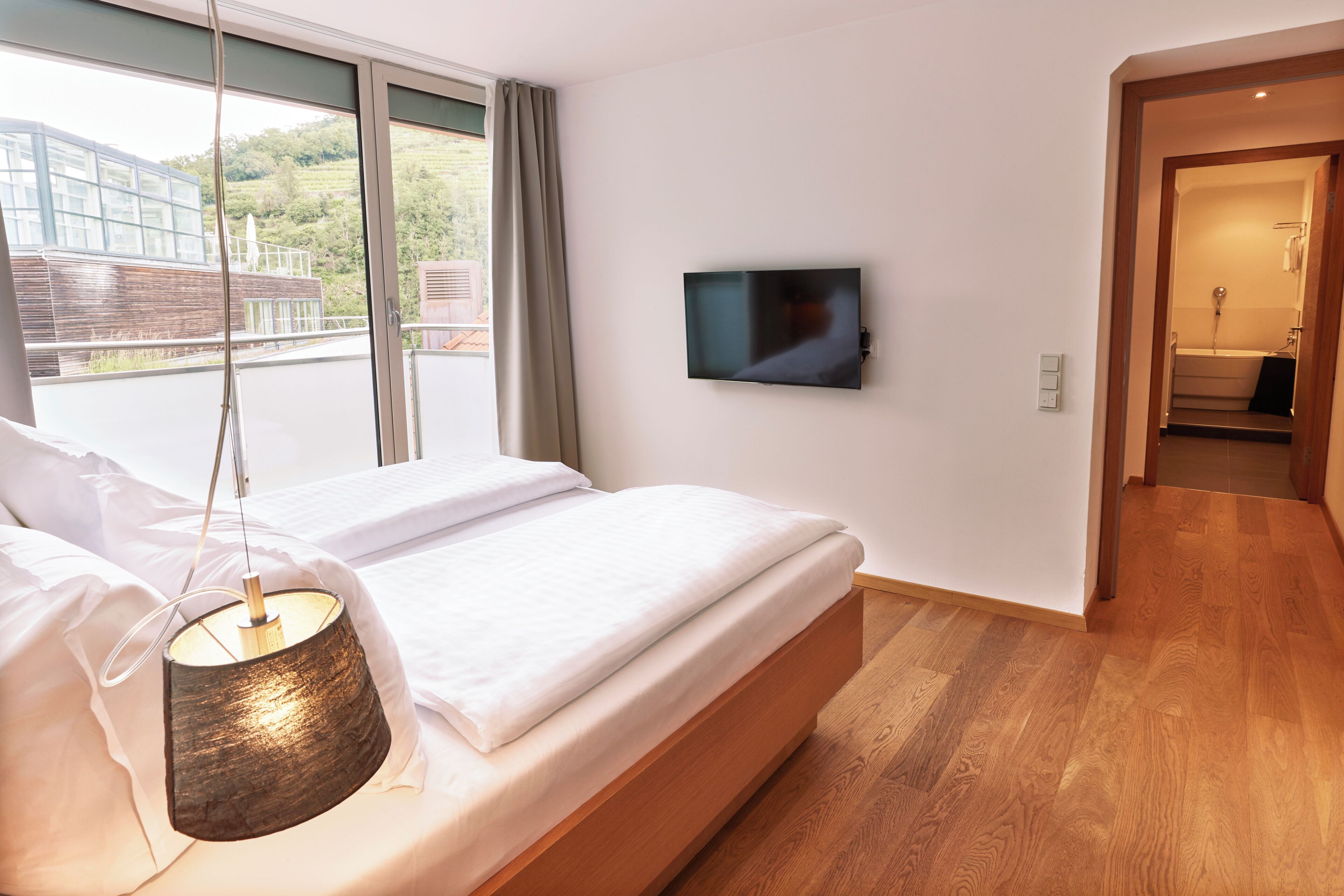 Una habitación de hotel moderna con una cama grande, un televisor montado en la pared y vistas al exterior a través del ventanal.