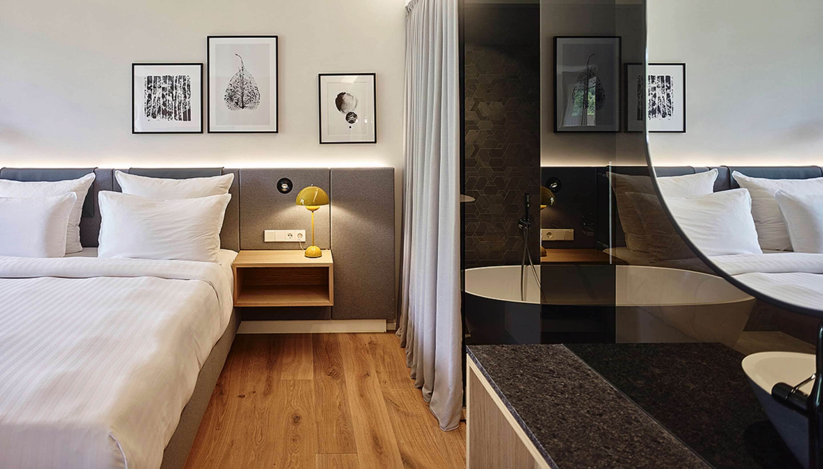 A hotel room with two beds, a bedside table with a lamp, a mirror, and artwork on the wall.