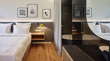A hotel room with two beds, a bedside table with a lamp, a mirror, and artwork on the wall.
