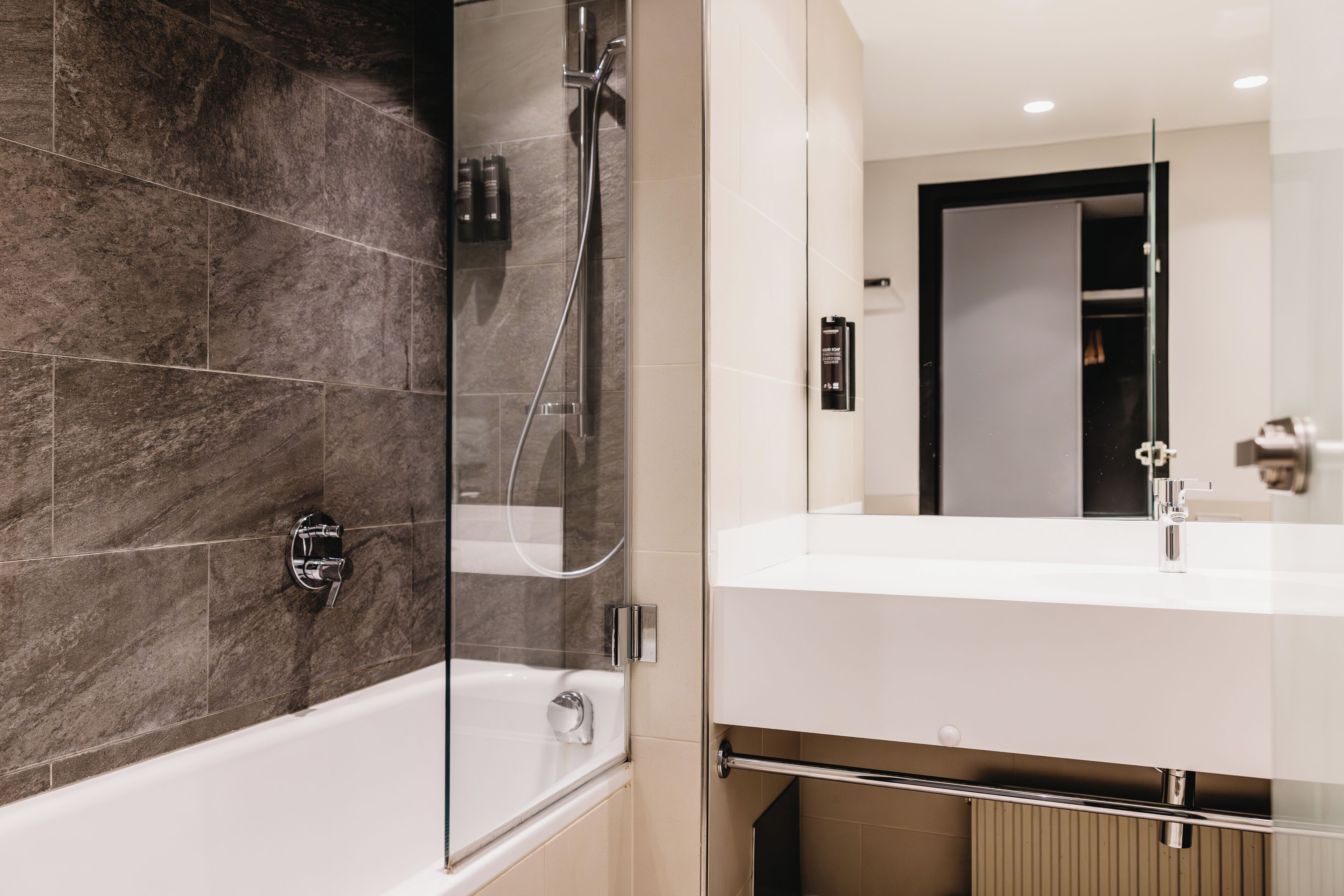 A modern bathroom with a glass-enclosed shower, a white bathtub, and a large mirror above a white sink.