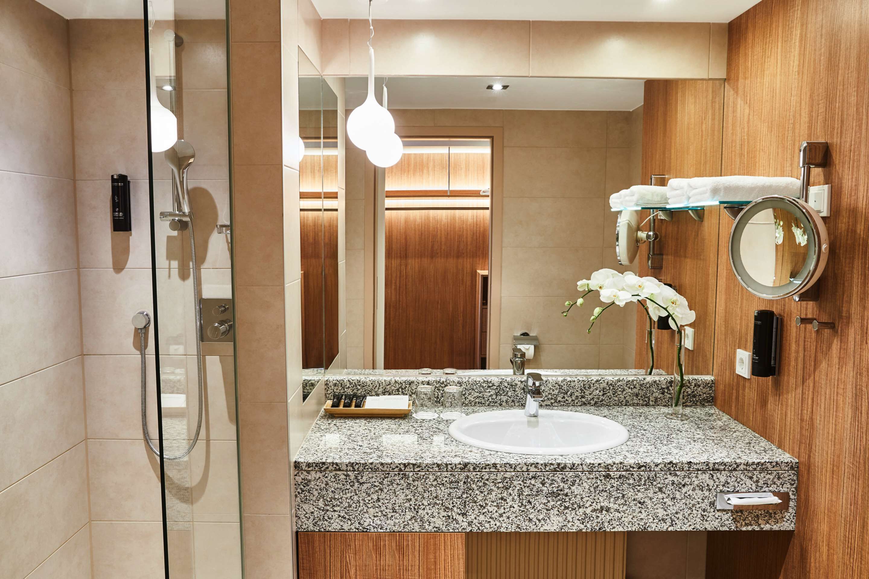 Un baño moderno con lavamanos de granito, cabina de ducha de vidrio y tocador de madera.