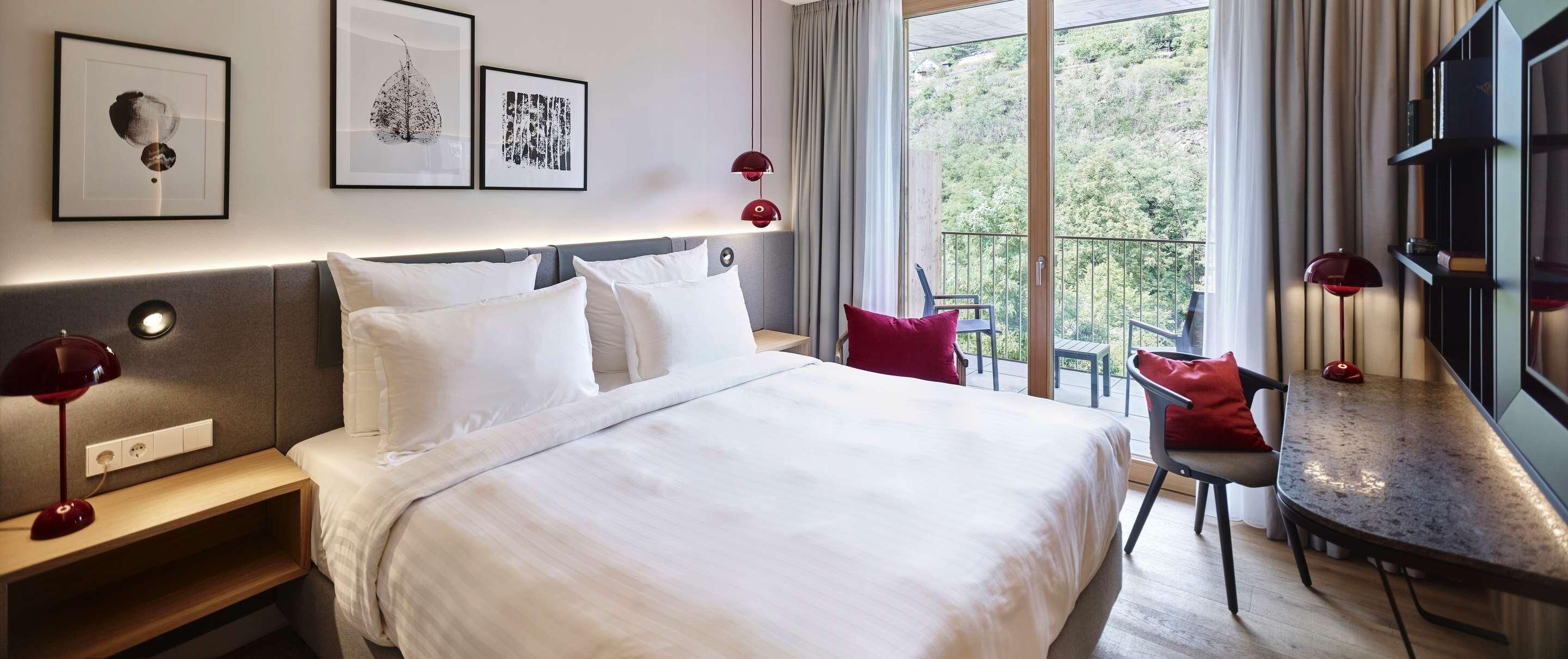 Una habitación de hotel con cama, mesitas de noche, escritorio y balcón con vistas.