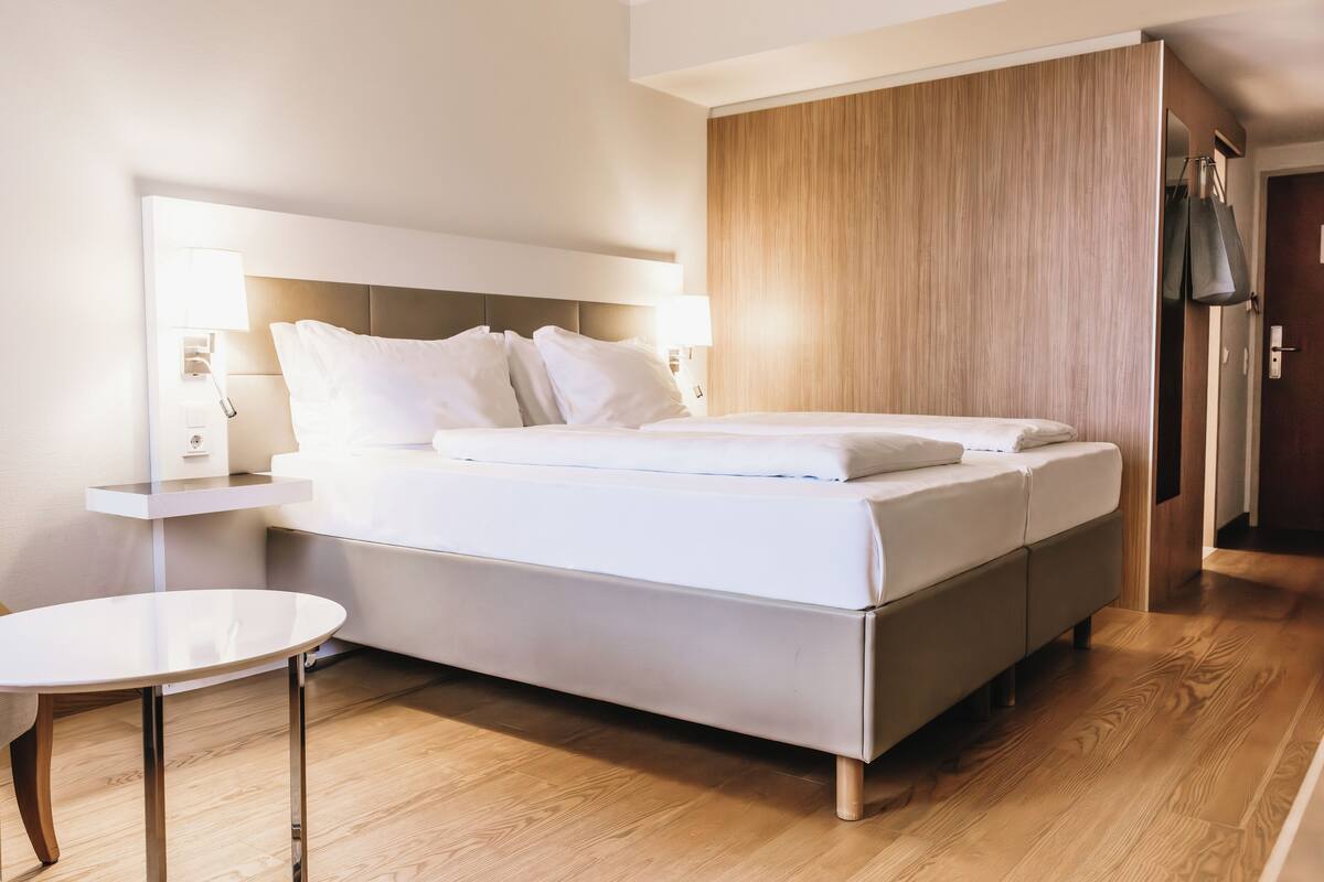 Habitación de hotel moderna con una cama grande, mesitas de noche, una pequeña mesa redonda y un armario de madera.