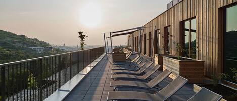 A rooftop terrace with sun loungers and a wooden building.