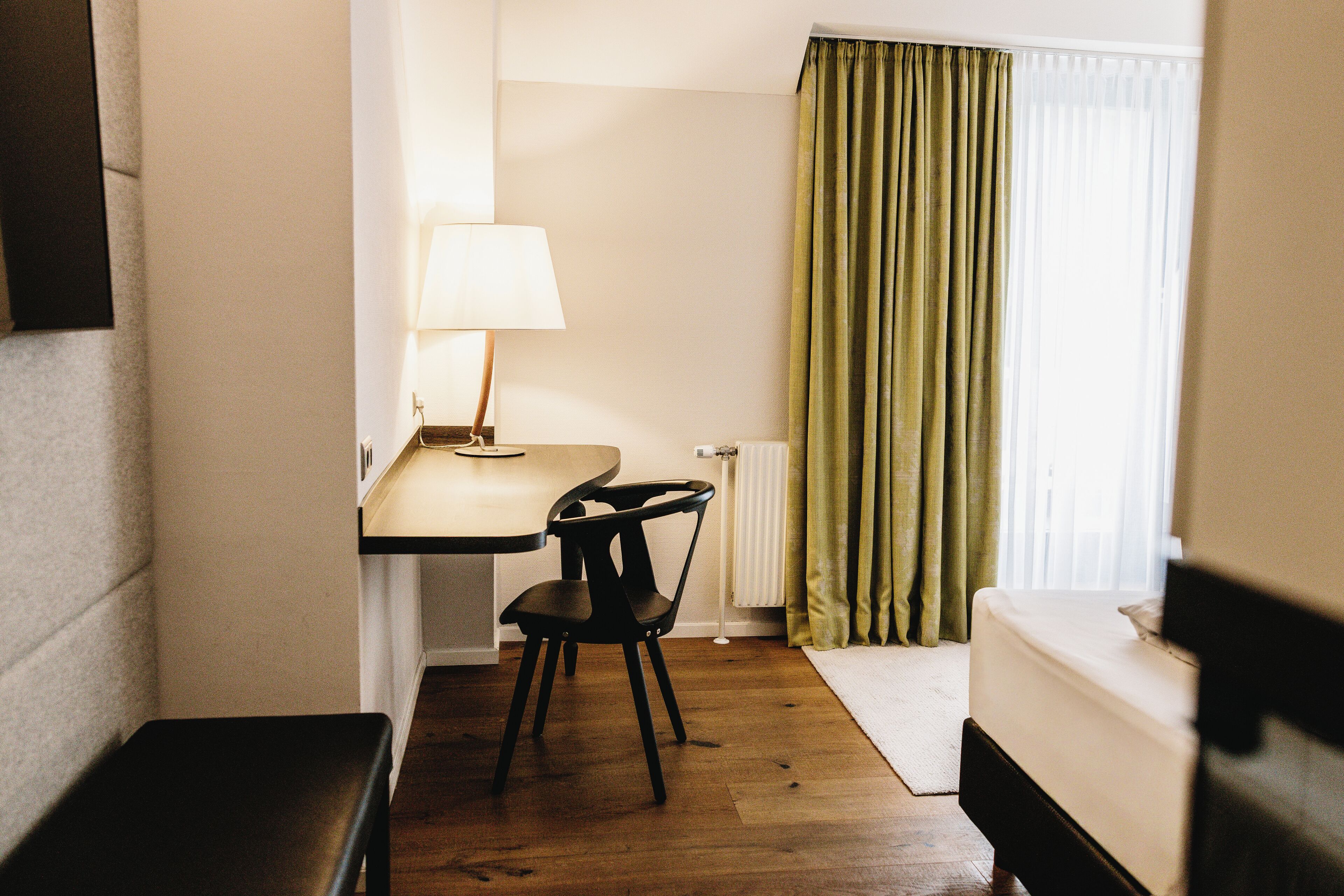 Una habitación pequeña y acogedora con cama, escritorio, silla, lámpara y ventana con cortinas.