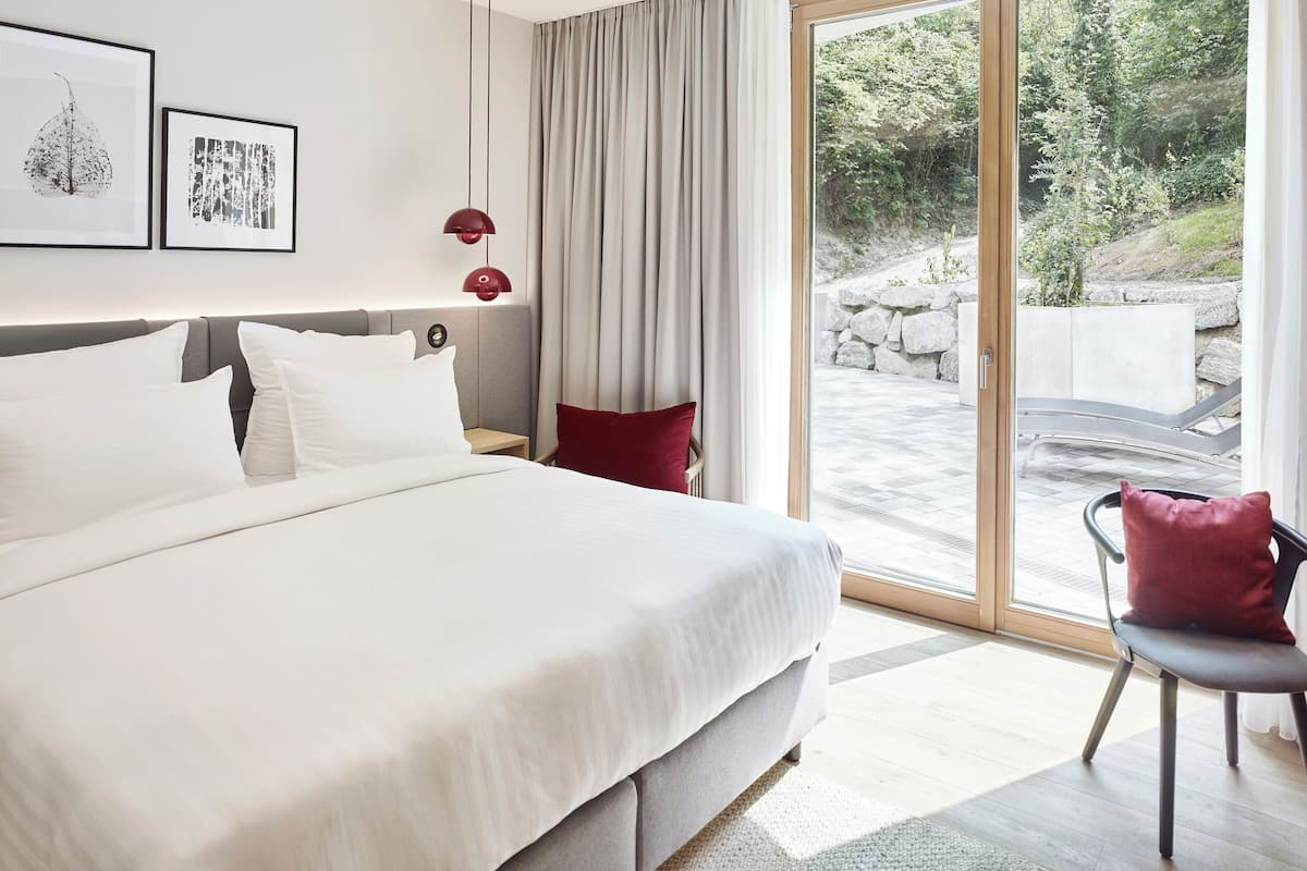 Una habitación de hotel moderna con una cama grande, un escritorio, una silla y vistas al exterior.