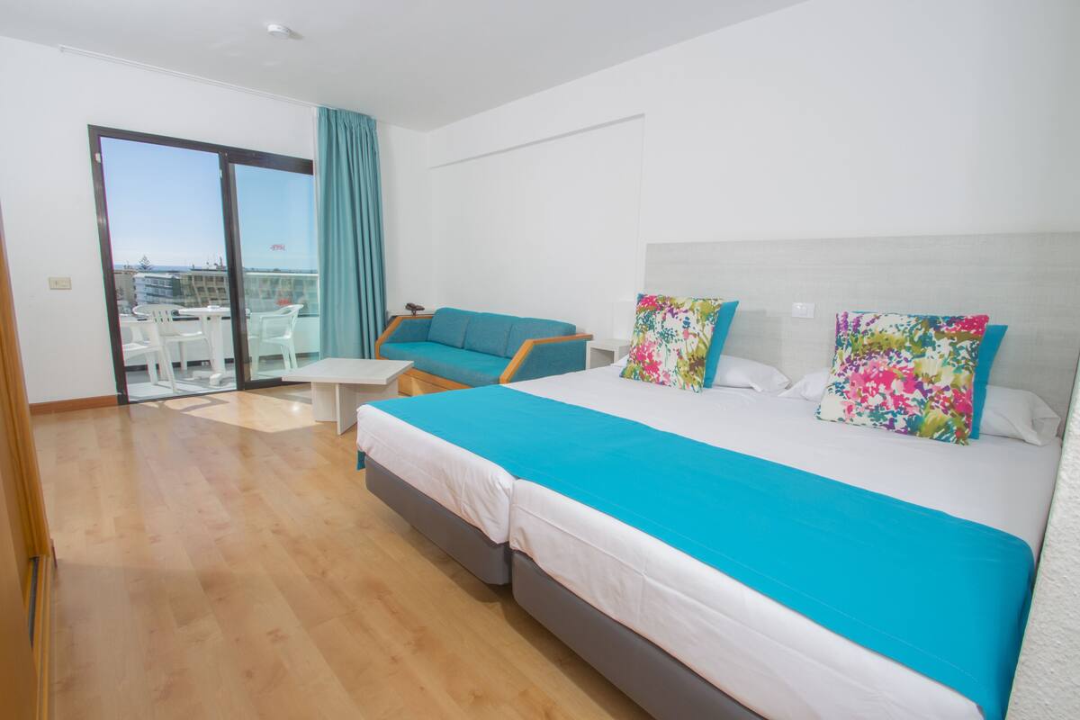 A hotel room with a large bed, a small table, a chair, and a balcony with a view.