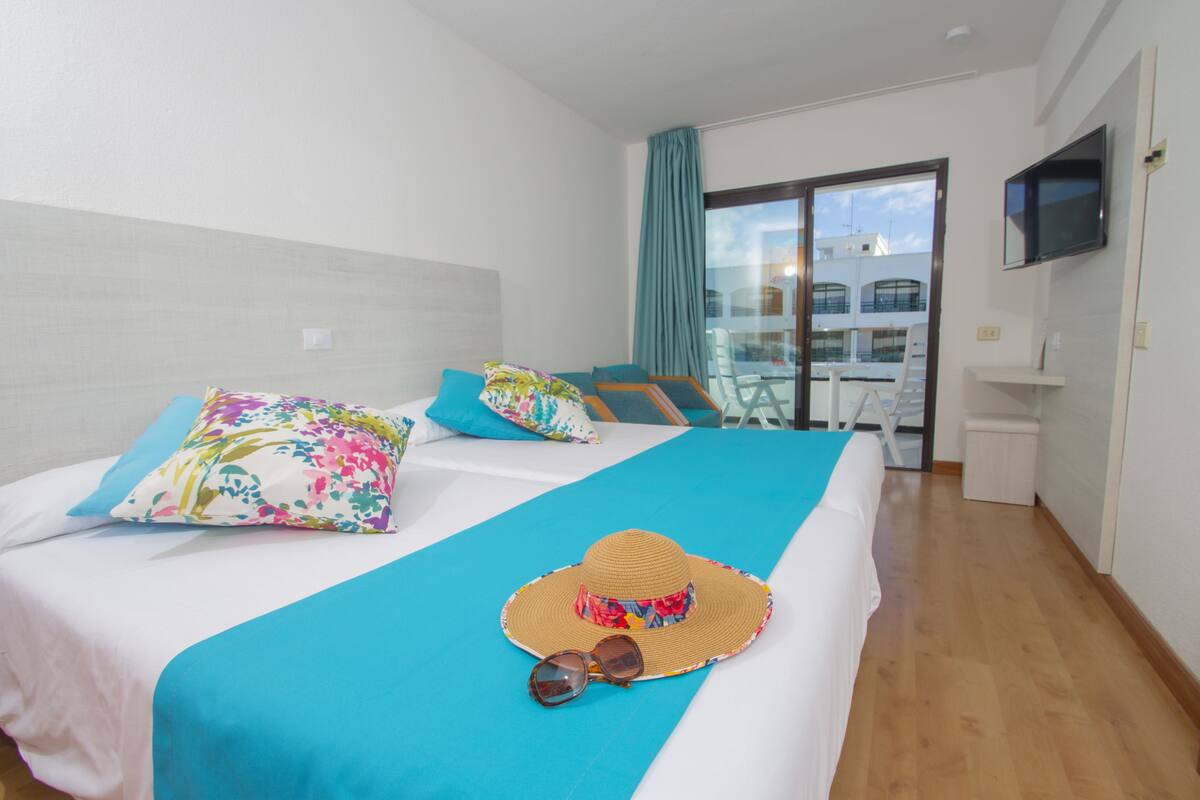 A hotel room with a bed, a balcony, a TV, and a view of buildings.