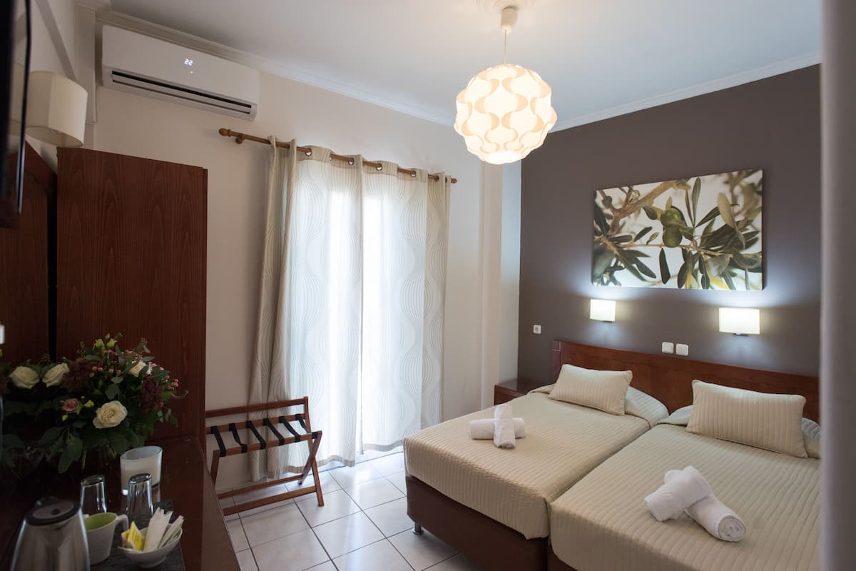Habitación de hotel con dos camas, un armario de madera, un escritorio con lámpara, un jarrón de flores y una lámpara en el techo.