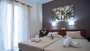 Habitación de hotel con dos camas, un ventanal grande con cortinas, una obra de arte en la pared y una mesita de noche con un florero.