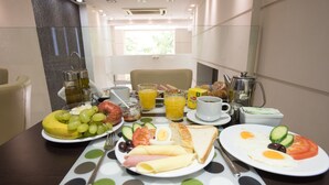 Una mesa de desayuno con platos de huevos, tostadas y fruta, una cafetera y una ventana con luz natural.
