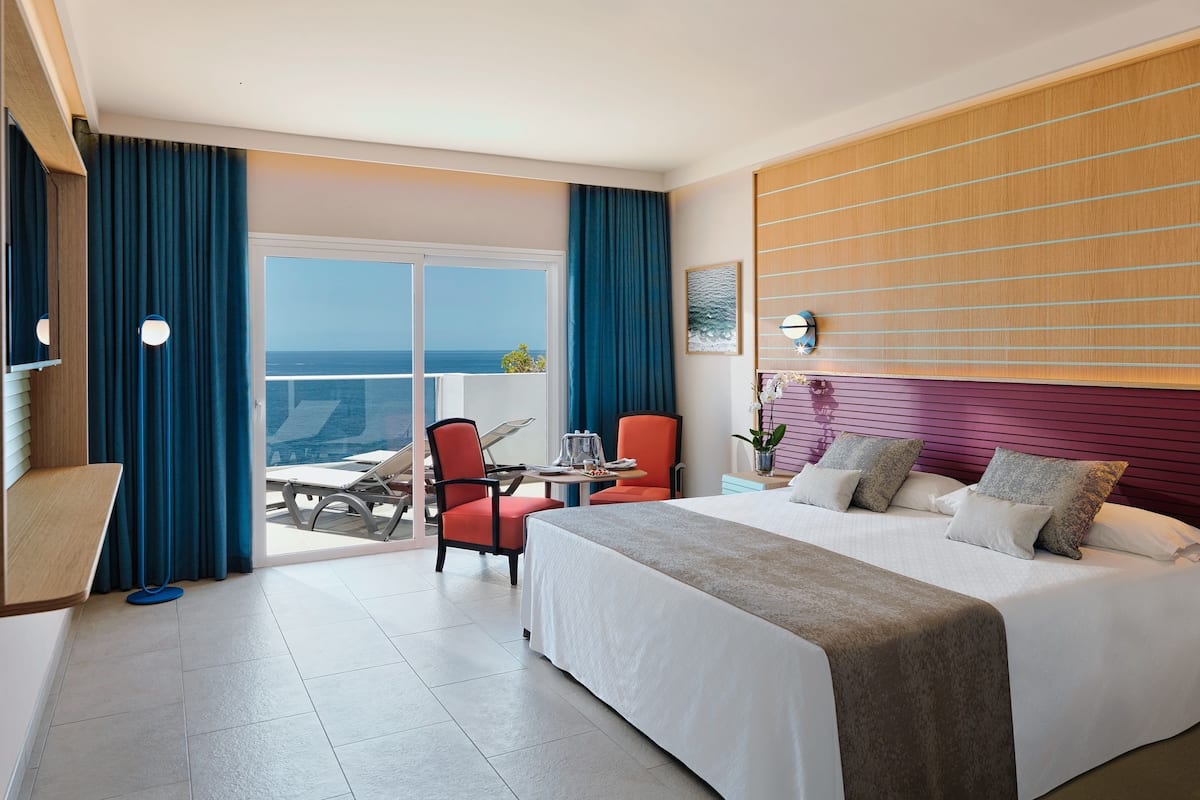 A hotel room with a large bed, a desk, a chair, and a view of the ocean.